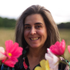 Porträtt på Maja Bohlemark. Hon står på ett öppet fält med blommor runt om sig.