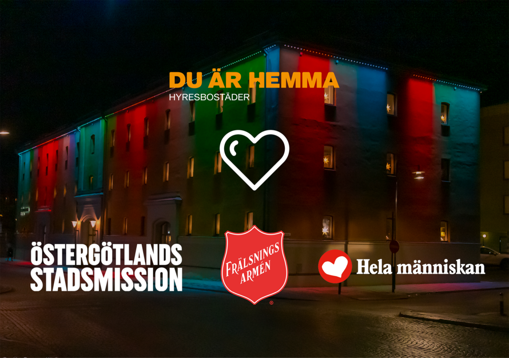 Bild på Hyresbostäders huvudkontor, fotograferad i mörkret med julig fasadbelysning. På bilden syns Hyresbostäders logga tillsammans med Östergötlands Stadsmission, Frälsningsarmén och Hela människan,