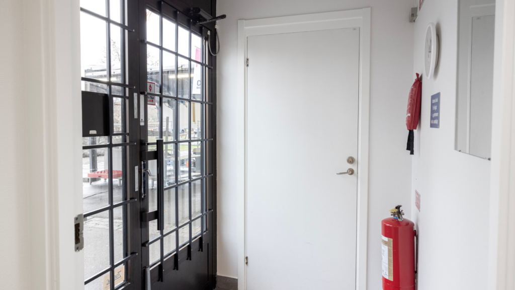 Interiörbild av kvarterslokal Sekreteraren: utrymme precis innanför entrédörren. Det finns en spegel,, brandsläckare och brandfilt.