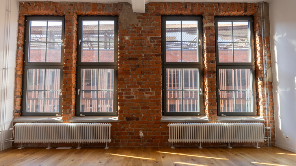 Interiörbild i fastighet Fabriken. Två stora industriella fönster längs en tegelvägg.