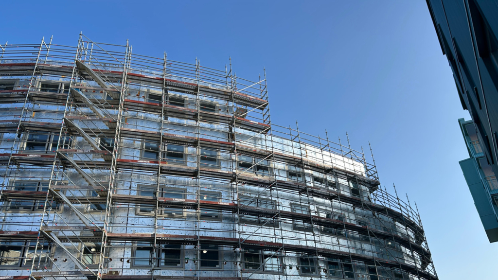 Bild på husbygge med byggnadsställningar. Huset är ovalt och har 3-4 våningar. Himlen i bakgrunden är klarblå utan moln.