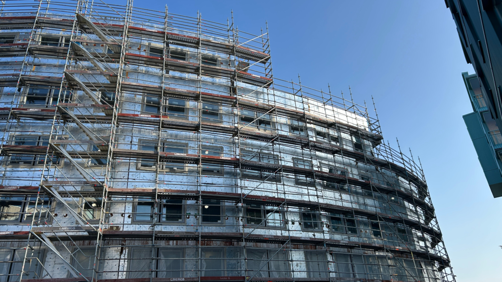 Bild på husbygge med byggnadsställningar. Huset är ovalt och har 3-4 våningar. Himlen i bakgrunden är klarblå utan moln.