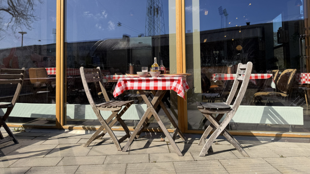 Stol och bord i trä på uteservering. Bordet har rödvitrutig duk