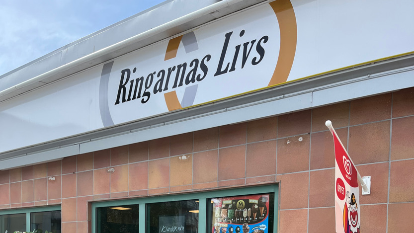 Affären Ringarnas Livs fotad utifrån, dörren är öppen, röd glassflagga fäst på den bruna kakel fasaden 