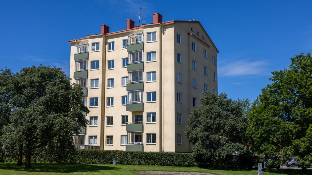 Fasaden på Apelgatan 8. Huset är ljusgult med gröna balkonger. I förgrunden finns flera träd.