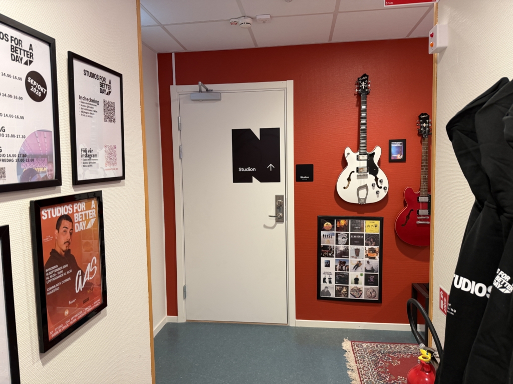 Röd vägg med vit, stängd dörr. På väggen hänger tavlor med svarta ramar och två elgitarrer